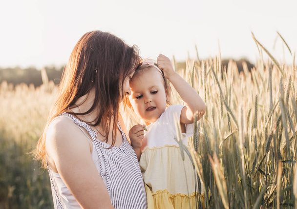 Mom holds her little daughter in her arms in a wheat field in the summer - Photo, Image