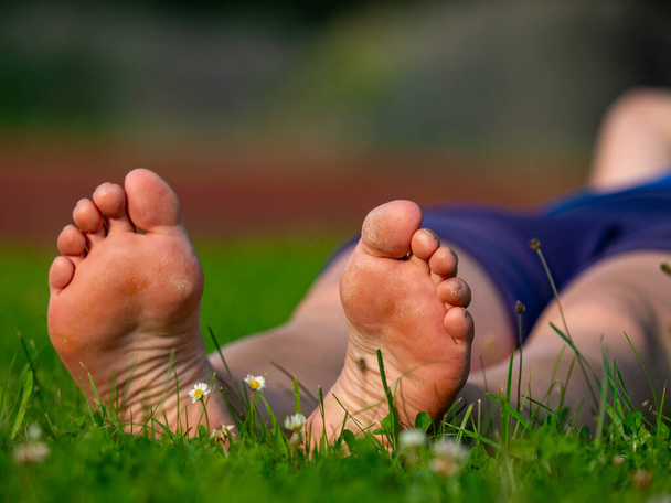 Senior woman sitting barefoot on grass in sunny summer, elderly female feet with rough skin - Foto, Imagem