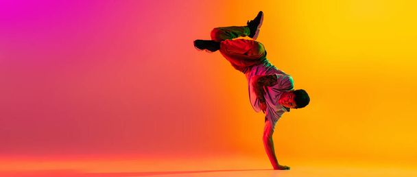 Flyer with young stylish man, break dancing dancer training in casual clothes isolated over gradient pink yellow background at dance hall in neon light. - Foto, Imagem