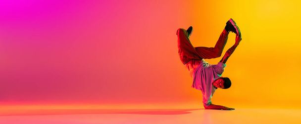 Flyer with young stylish man, break dancing dancer training in casual clothes isolated over gradient pink yellow background at dance hall in neon light. - Photo, image