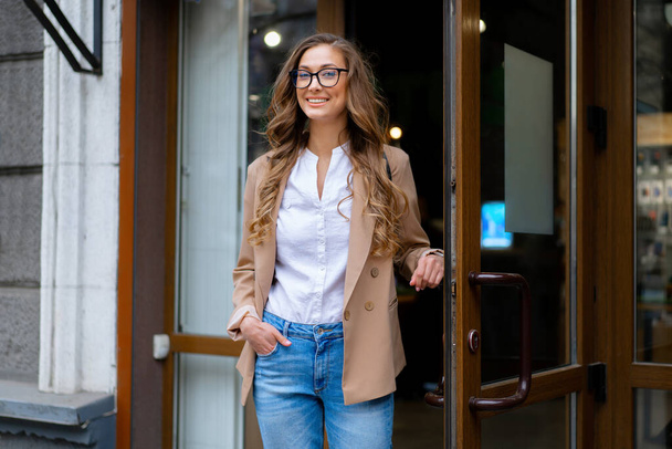 Business Woman Come Out Store Door Outside Caucasian Female Business Person Standing Near Shop Doorway Dressed Blue Jeans Jacket Glasses Holding Doorhandle - Fotografie, Obrázek
