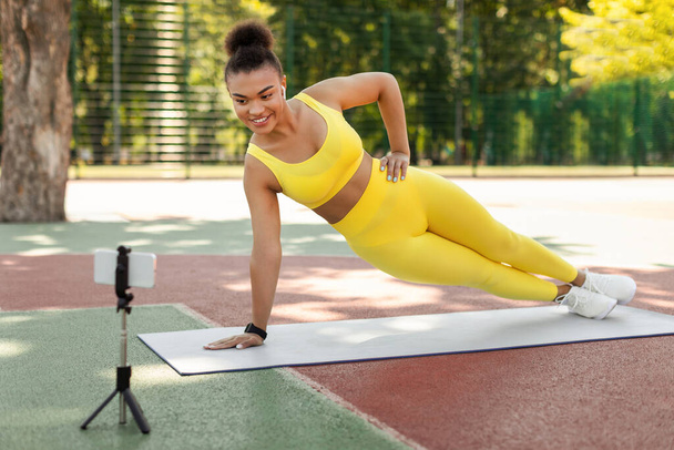 Online-Workout. Junge schwarze Frau plankt vor Smartphone - Foto, Bild
