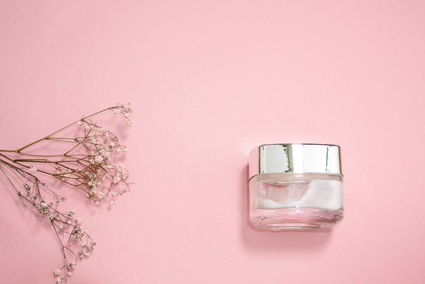 kosmetyki płaskie: kosmetyki do twarzy na jasnoróżowym tle z suchymi kwiatami  - Zdjęcie, obraz