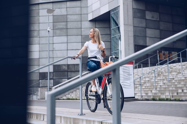 Όμορφη και χαμογελαστή ενήλικη γυναίκα απολαμβάνουν ποδήλατο βόλτα στην ηλιόλουστη αστική υπαίθρια δραστηριότητα αναψυχής στην πόλη . - Φωτογραφία, εικόνα