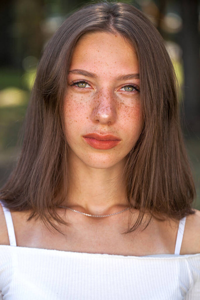 Portrait of a young beautiful brown-haired girl with freckles on her face - Valokuva, kuva