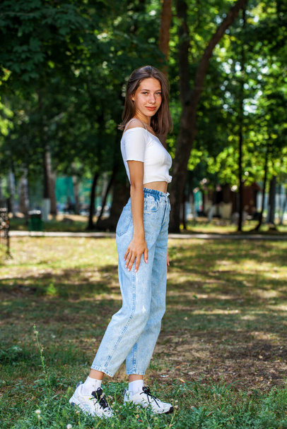 Full length portrait, young beautiful girl in blue jeans posing in a summer park - Fotografie, Obrázek