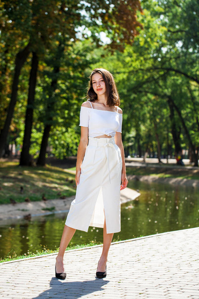 Full-length portrait, a young beautiful girl in a white skirt posing in a summer park - Zdjęcie, obraz