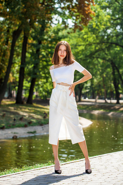 Full-length portrait, a young beautiful girl in a white skirt posing in a summer park - Фото, зображення
