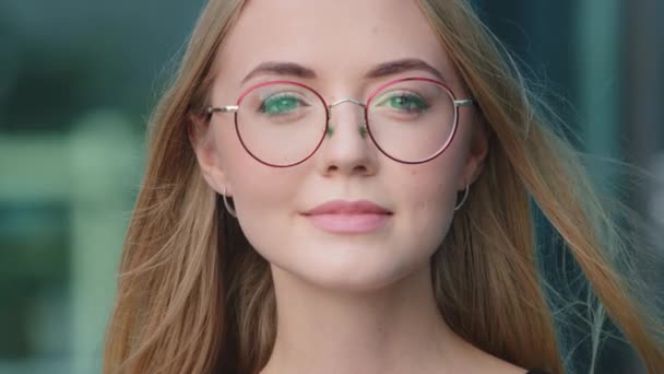Gözlüklü gülümseyen milenyum kadınının yakın plan portresi mavi stüdyo arka planında izole edilmiş poz veren mutlu beyaz İskandinav kadın model gözlüklü kameraya bakın - Video, Çekim