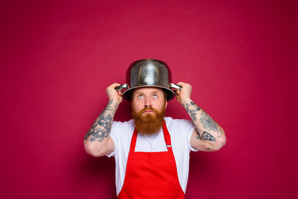 preocupado chef con barba y delantal rojo juega con olla - Foto, imagen