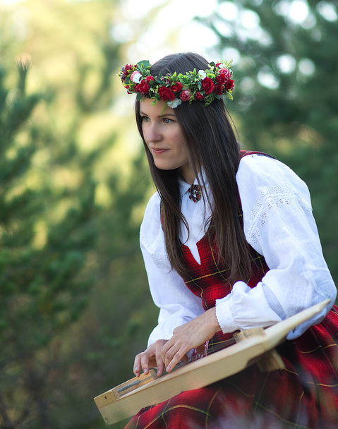 Retrato de uma mulher com uma harpa Bela fêmea de cabelos castanhos com uma coroa de flores na cabeça, vestindo um traje nacional tocando harpa na floresta - Foto, Imagem