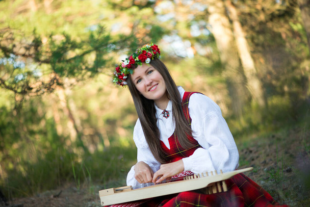 ハープを持つ女性の肖像頭に花の花輪を持つ美しい茶色の髪の女性は、森の中でハープを演奏する民族衣装を着て - 写真・画像
