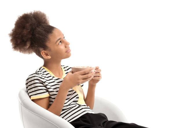 African-American teenage girl with cup of hot cacao sitting on chair against white background - 写真・画像