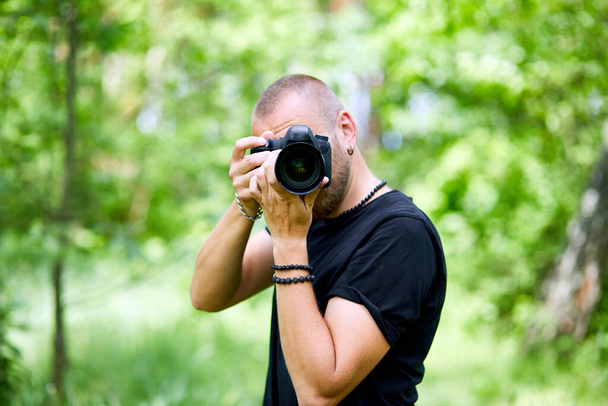 屋外でカメラで顔を覆う男性写真家の肖像写真、世界の写真家の日、手にカメラを持った若い男. - 写真・画像