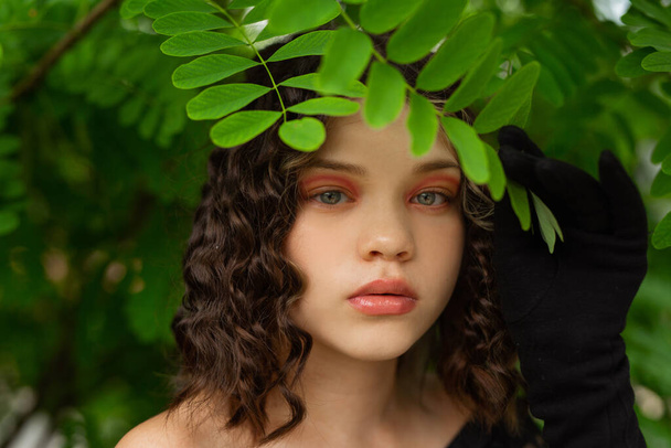 beautiful young well-groomed female face with makeup near green leaves - Foto, Imagem