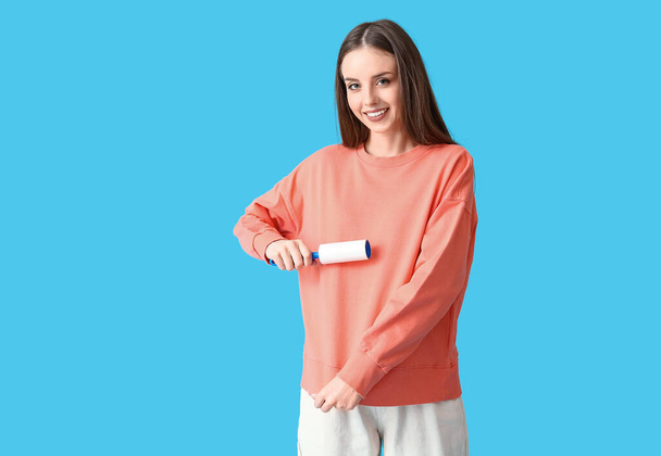 Young woman cleaning her sweatshirt with lint roller on color background - 写真・画像