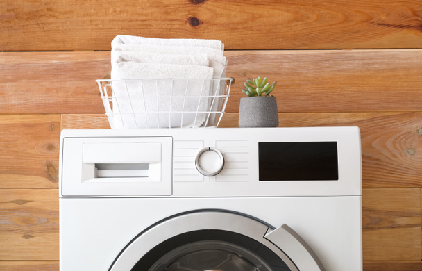 Máquina de lavar roupa moderna com toalhas perto da parede de madeira - Foto, Imagem
