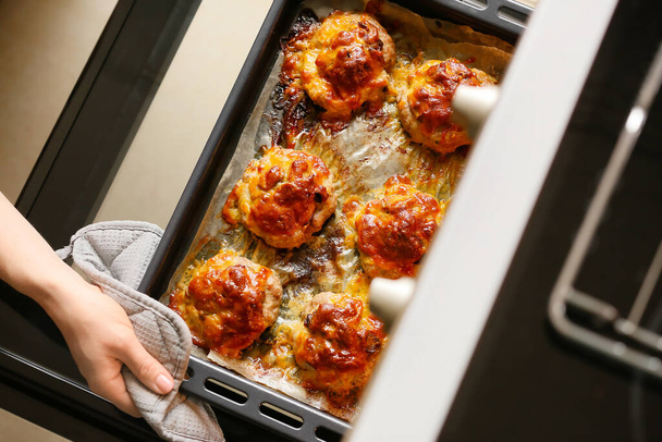 Frau holt Backblech mit Hackfleisch, Pilzen und Käse aus dem Ofen - Foto, Bild