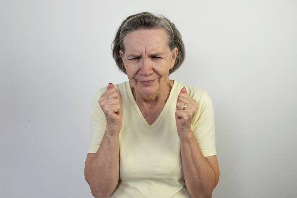 anciana mujer senior camisa pared blanco fondo infeliz triste miedo mano emoción retirado dolor de cabeza migraña estrés aterrorizado - Foto, imagen