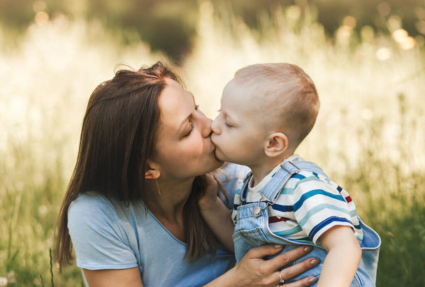 Mały chłopiec maluch całuje swoją matkę w przyrodzie w lecie - Zdjęcie, obraz