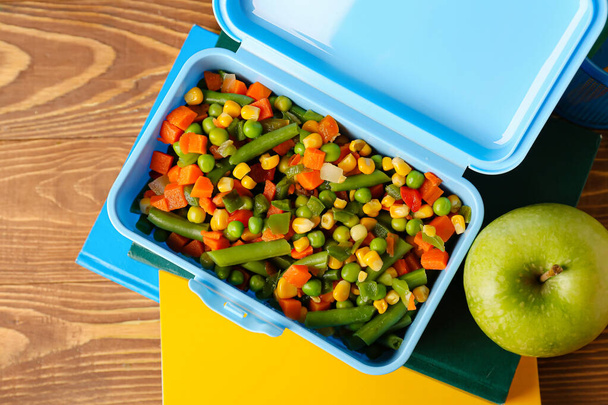 Lunchbox with vegetables, apple and notebooks on wooden background, closeup - Fotoğraf, Görsel