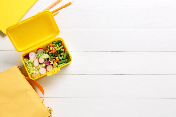 Обідня коробка з овочами, сумкою та канцелярськими товарами на світлому дерев'яному фоні
 - Фото, зображення