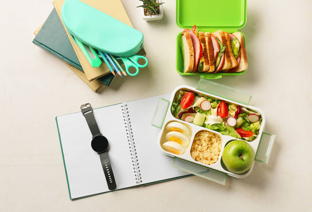 Lunch boxes with tasty food, wrist watch and stationery on light background - Photo, Image