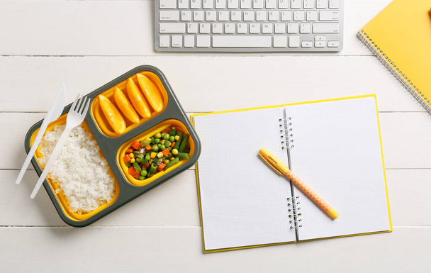 Γεύμα κουτί με νόστιμο φαγητό, σημειωματάριο, στυλό και πληκτρολόγιο σε ανοιχτό ξύλινο φόντο - Φωτογραφία, εικόνα