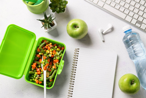 Lunchbox met groenten, notebook, oortjes, flesje water en toetsenbord op lichte achtergrond - Foto, afbeelding