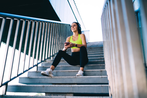  Young slim woman in active wear training on stadium doing squats exercises for lower body strength,caucasian girl keeping fitness goals having workout for energy wellness listen music in headphones - Fotografie, Obrázek