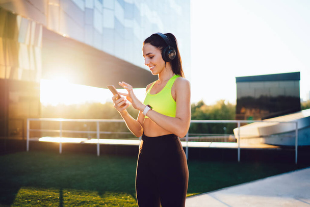  Young slim woman in active wear training on stadium doing squats exercises for lower body strength,caucasian girl keeping fitness goals having workout for energy wellness listen music in headphones - Valokuva, kuva