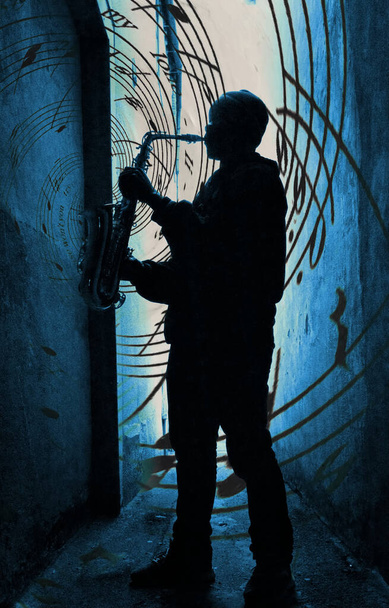  уличный саксофонист силуэт против синего света с музыкой, льющейся с саксофона - Фото, изображение