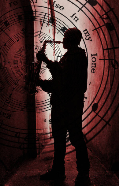  ένας παίκτης του δρόμου sax silhouetted aganst ένα κόκκινο φως με τη μουσική χυθεί από το σαξόφωνο - Φωτογραφία, εικόνα