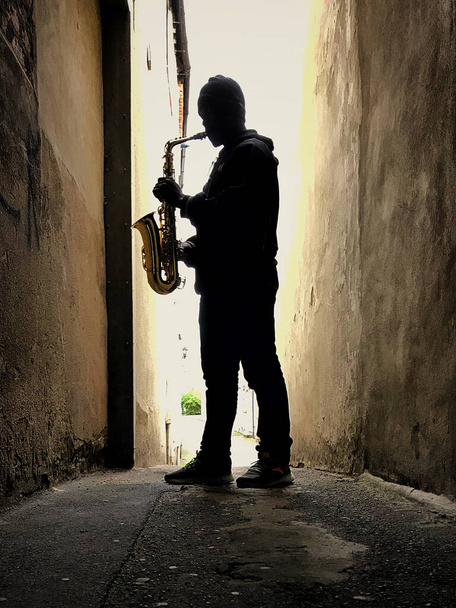Straatsaxofonist staat rechtop en is silhouetted tegen geel licht - Foto, afbeelding