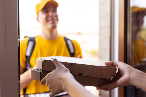 Young deliveryman in yellow uniform delivers order to clients, customers, buyers. Work, career, different professions concept. Idea of convenience, speed, comfort, safety, service. - Photo, Image
