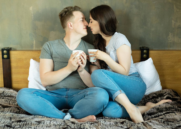 Stay at home concept, lifestyle theme. Young man and woman with cups on bed. - Fotografie, Obrázek