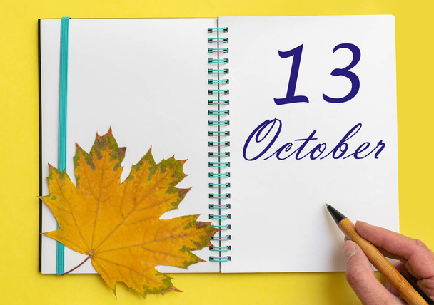 Trzynasty dzień października. Ręczne pisanie daty 13 października w otwartym notatniku z pięknym naturalnym liściem klonu na żółtym tle. Jesienny miesiąc, koncepcja dnia roku. - Zdjęcie, obraz