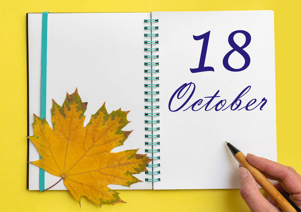 18th day of october. Hand writing the date 18 october in an open notebook with a beautiful natural maple leaf on a yellow background. Autumn month, day of the year concept. - Fotó, kép