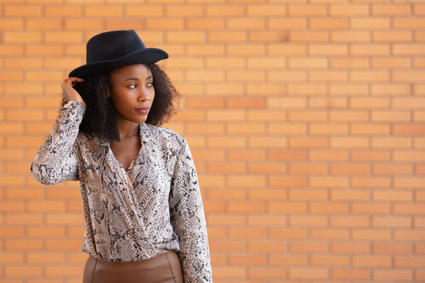 Portrait of a stylish woman with a black hat on a brick wall background - Foto, Bild
