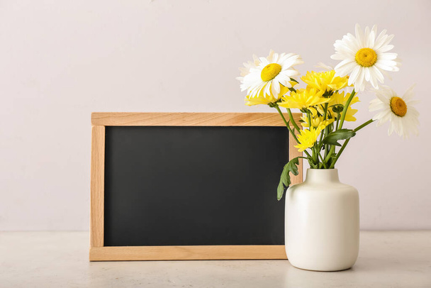 Vase with flowers and blackboard on light background. Teacher's Day celebration - Photo, Image