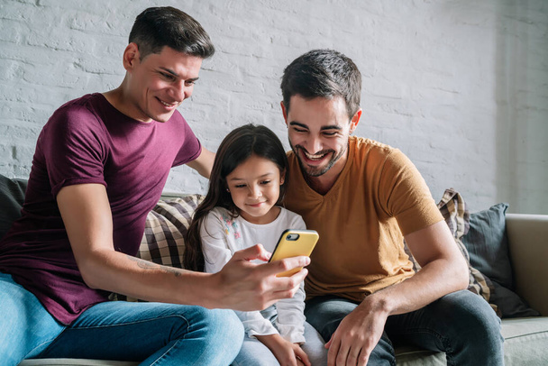 Gay couple and their daughter using a mobile phone at home. - Foto, imagen