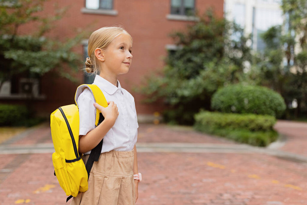 Schoolgirl back to school after summer vacations. Child in uniform standing early morning outdoor.  - 写真・画像