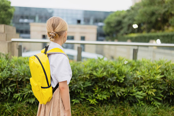 Schoolgirl back to school after summer vacations. Child in uniform standing early morning outdoor.  - Foto, Imagen