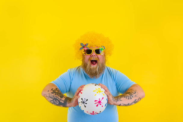 Hombre gordo con peluca en la cabeza y gafas de sol divertirse con una pelota - Foto, imagen