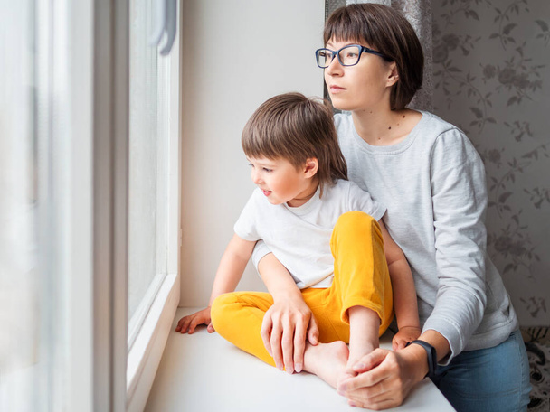 Sad woman looks at window. Forced stay at home because of coronavirus COVID-19 quarantine pandemic. Mother and son. Mom and child. - Valokuva, kuva