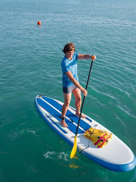 Paddle boarder. Sportsman paddling on stand up paddleboard. SUP surfing. Active lifestyle. Outdoor recreation. Vacation on seaside. - Photo, image