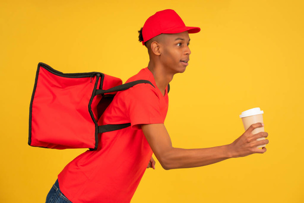 Young delivery man in red uniform running with a takeaway coffee. - Photo, Image
