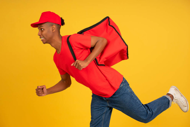 Young delivery man in red uniform running over isolated background. - Fotó, kép