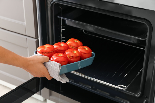オーブンで調理されていないトマトとベーキング皿を置く女性,クローズアップ - 写真・画像