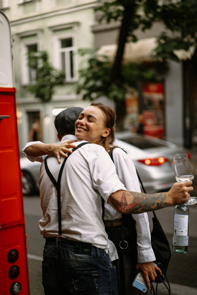 A young man in a white shirt and a cap with a woman on the street drinks wine from glasses. Friends meeting - Fotoğraf, Görsel